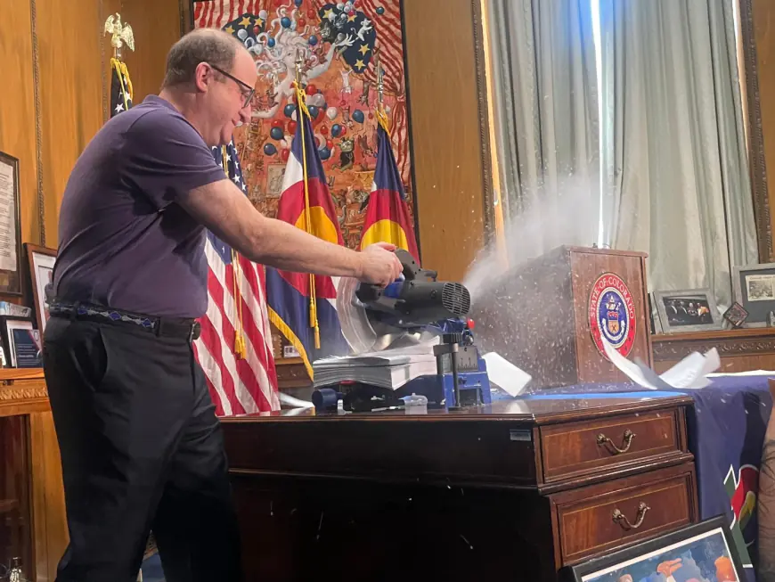 Gov. Jared Polis cuts through executive orders — wielding a circular saw on his desk